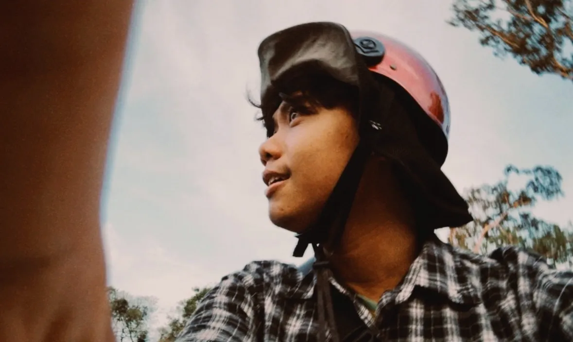 Vichet smiling in a red helmet and checked shirt, looking up at the sky